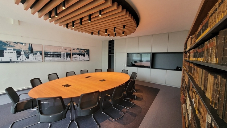 Blick in den neuen Mediationsraum mit ovalem Besprechungstisch und formgleichem Deckensegel aus Holzlamellen